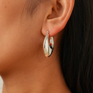 Detailed close-up of a high-polish silver teardrop hoop earring worn by a model