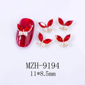 Detail of 3D alloy butterfly nail charm with red crystals and pearls on red manicured nail