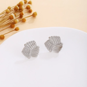 Close-up of silver knot stud earrings with twisted texture on a white display stand