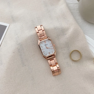 Macro shot of rose gold square quartz watch with steel strap and matching ring on linen fabric
