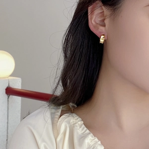 Detail view of a gold geometric textured earring worn by a model in soft lighting