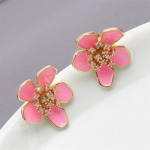 Macro detail of gold flower stud earrings with pink enamel petals and zircon centers