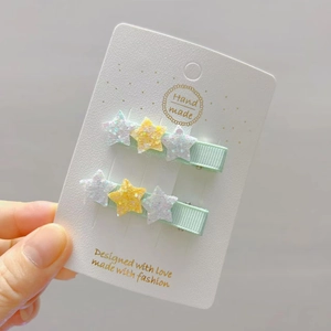 Close-up of two light green ribbon hair clips with glitter stars on a display card