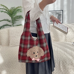 Detail of red plaid tote bag with 3D plush puppy and pink bow held by a model