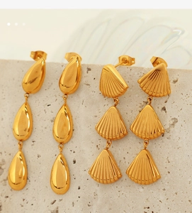 Detail of gold water drop and tiered shell shaped earrings on a textured stone base