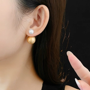 Close-up of pearl and brushed gold metal ball stud earring worn by a model
