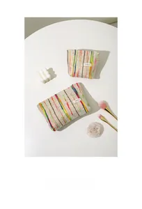 Détail de trousses de toilette tissées à rayures sur fond blanc minimaliste