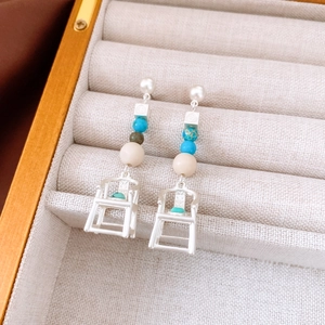 Detailed close-up of long drop earrings featuring white pearls and a silver chair pendant