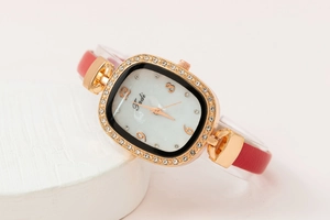 Gros plan d'une montre en cuir rouge avec lunette en strass or rose sur pierre blanche