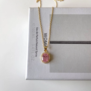 Macro shot of oval pink zircon pendant with gold pavé halo on a fine chain