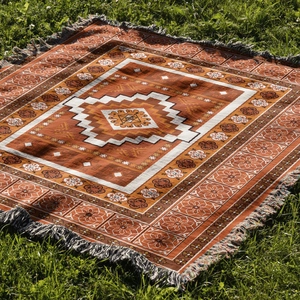 Close-up of bohemian woven camping blanket with tribal patterns and tassels on green grass