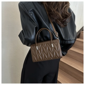 Detailed view of a brown quilted crossbody bag shown on a model on wooden stairs