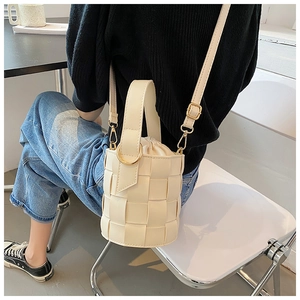 Detail of woven bucket bag featuring cream faux leather texture and gold chain strap