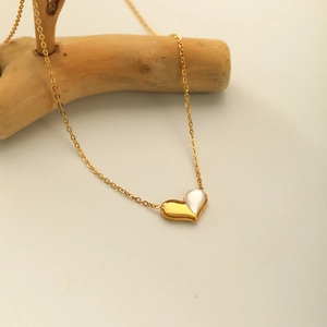 French design heart necklace with gold finish and white shell inlay on wooden stand