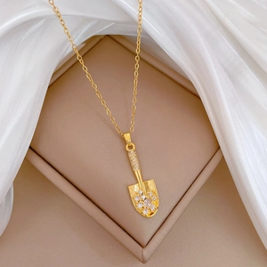 Close-up of golden shovel pendant with sparkling cubic zirconia on a silk background