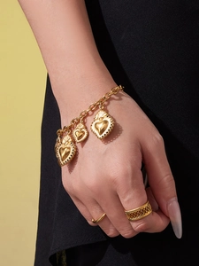 Détail du bracelet cœur en acier doré 18 carats et des bagues sur le poignet du mannequin