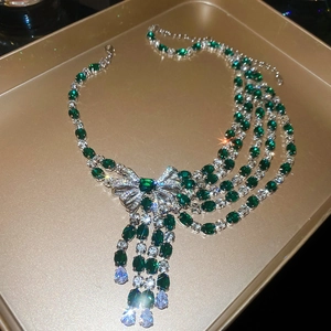Detail of silver bow necklace with emerald green stones and cascading tassel pendants