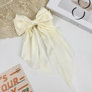 Macro view of creamy white satin oversized bow hair clip on a minimalist lace background