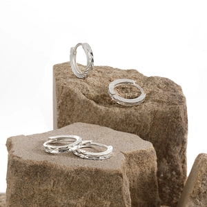 Polished S990 silver hoop earrings with diamond-cut texture on a natural stone base