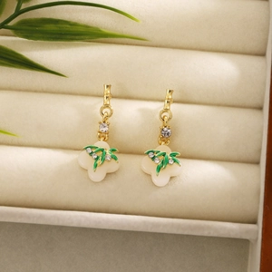 Macro shot of long bamboo tassel earrings with white petal pendants and green leaves