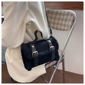 Detailed shot of black suede handbag featuring faux fur trim and gold buckle straps