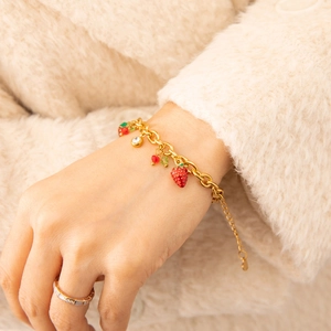 Detailed close-up of a gold strawberry charm bracelet with red crystal and green accents