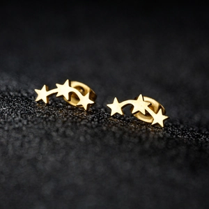 Boucles d'oreilles minimalistes en acier doré à trois étoiles sur fond noir texturé