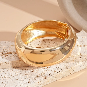 Dettaglio del bracciale ovale dorato irregolare con cerniera a molla e finitura lucida