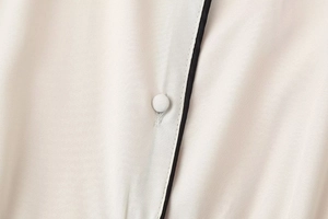 Détail de robe chemise beige sans manches avec liseré noir et bouton recouvert de tissu