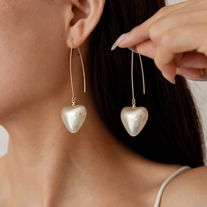 Elegant gold drop earrings with pearl heart pendants worn by a model in a natural setting