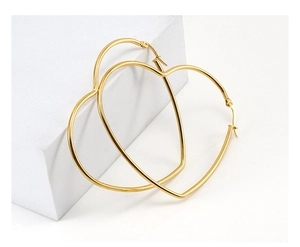 Close-up of polished gold heart hoop earrings on a white minimalist geometric block