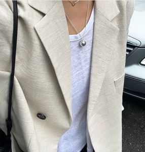 Close-up of a minimalist silver ball pendant necklace styled with a golden choker on a model