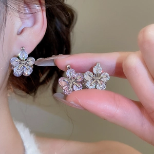 Detail showing zirconia flower earrings on model and hand for jewelry scale