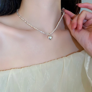 Close-up of split silver chain and pearl necklace with 3D heart pendant on collarbone