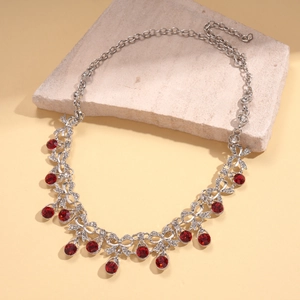Close-up of vintage silver necklace with red crystals and intricate vine pattern details