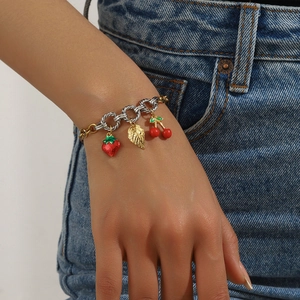 Close-up of gold and silver layered strawberry cherry charm bracelet on denim