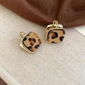 Dettaglio di orecchini quadrati dorati con trama leopardata in peluche su sfondo lino