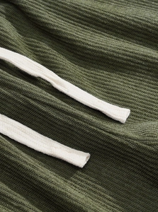 Detail of green corduroy joggers showing ribbed texture and cream-white braided drawstrings