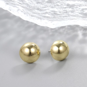 Macro shot of mirror-polished gold sphere stud earrings with water ripple reflection