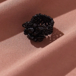 Detailed view of a black beaded wide ring on textured purple satin fabric with shadows