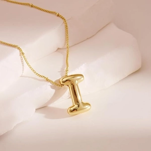 Detail of 18K gold balloon letter 'I' pendant on beaded chain with polished finish