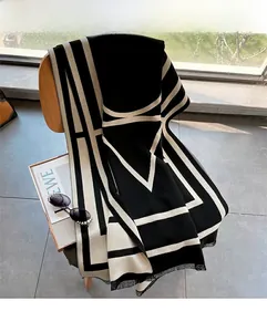 Detail of a thick knit scarf with geometric OM patterns and fringe on a wooden chair