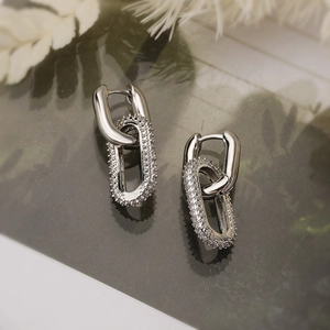 Orecchini geometrici in argento dorato con zirconi pavé su sfondo naturalistico