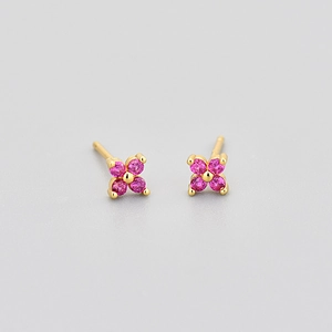 Detailed macro shot of small gold earrings with four pink-purple zirconia flower petals