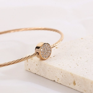 Detail of rose gold twisted cable bracelet featuring a round pavé zircon charm on stone