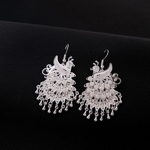 Detailed close-up of peacock-shaped silver earrings with intricate hollow-out metalwork