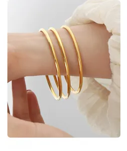 Dettaglio di tre bracciali in acciaio al titanio dorato lucido indossati al polso, lucidi