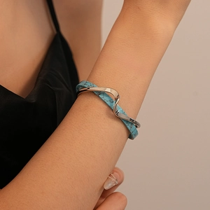 Detail of silver wavy bangle with blue faux turquoise inlay worn on a female wrist