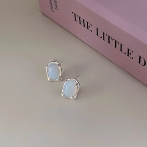 Detail of irregular silver stud earrings with translucent light blue gemstones and texture