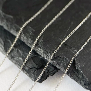Macro shot of fine silver-toned stainless steel link chains on black textured rock